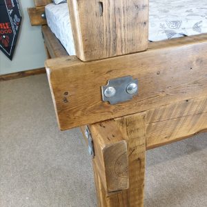 A grand, monolithic medieval bed crafted from raw, weathered 200-year-old wood, highlighting the exceptional rustic texture and heavy-duty construction.