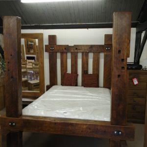 A rustic four-poster medieval bed crafted from reclaimed wood, showcasing a sturdy and timeless design.