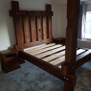 A large king-size bed, featuring a chunky medieval bed frame expertly handcrafted from reclaimed wood with a rich, dark finish.