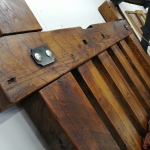 A large, four-poster medieval bed frame handcrafted from aged reclaimed timber, with a rustic and imposing design that emphasizes its solid, heavy-duty construction.