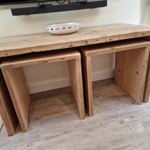 A full-height view of the rustic nesting tables, showcasing the unique proportions of each piece as they are stacked together. The solid construction and rich texture of the reclaimed wood are highlighted, with light catching the natural imperfections and showcasing the handcrafted quality.