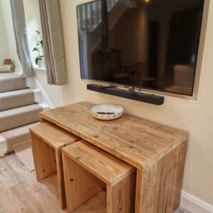 A rustic nesting tables set, crafted from reclaimed wood, is shown from a different angle, revealing a close-up of the smooth, polished surface and the natural markings of the timber. The varying heights of the tables are visible, demonstrating their practical and aesthetic appeal.